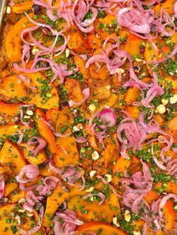 Plat végétarien coloré avec des tranches de courge, oignons rouges marinés, herbes fraîches et noisettes concassées.