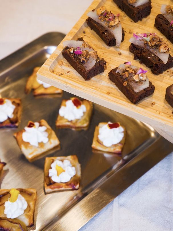 Assorted bite-sized desserts on wooden and metal trays, including chocolate and cream-topped pastries.