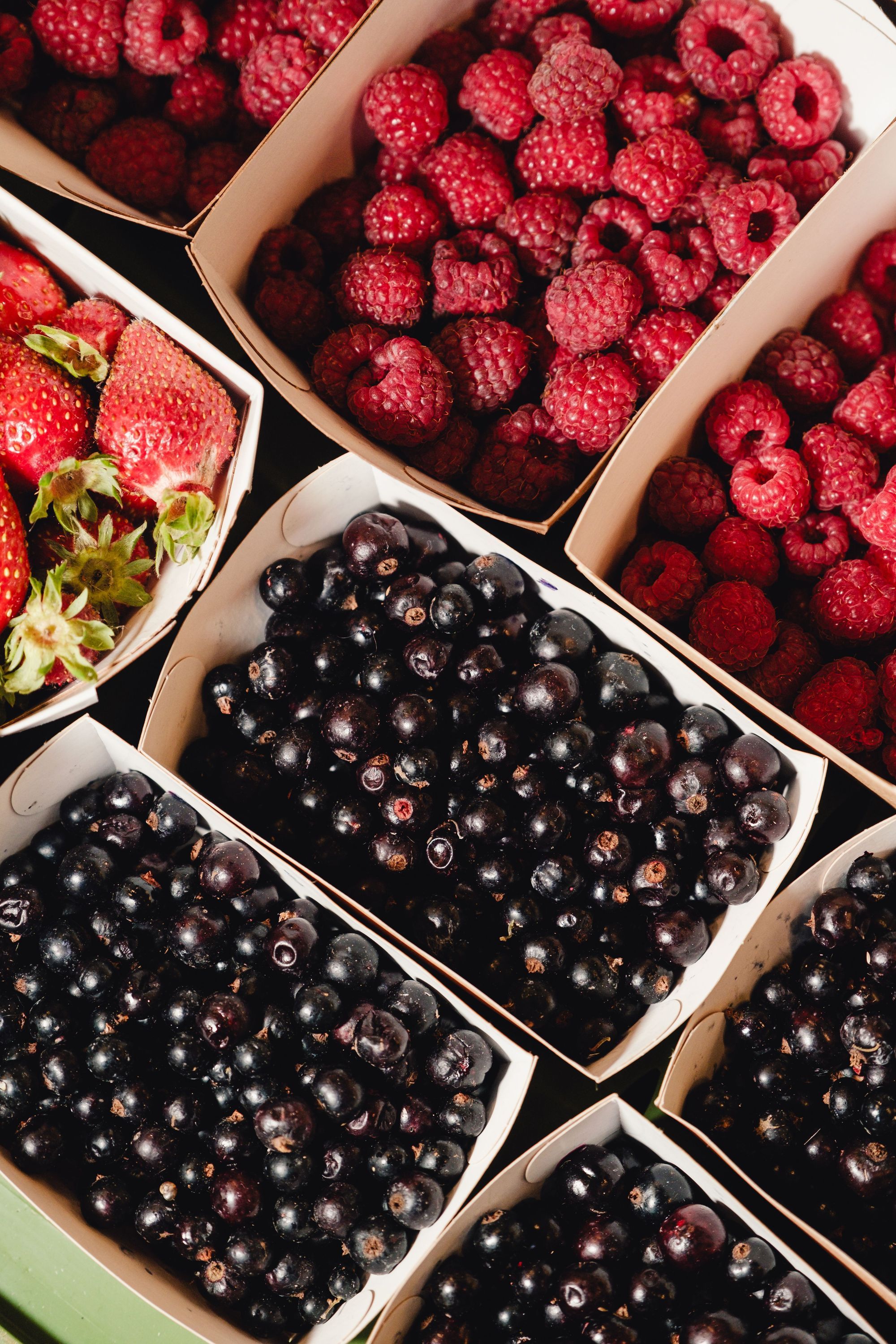 Fruits rouges frais comme des framboises, fraises et baies noires présentés dans des contenants en carton.