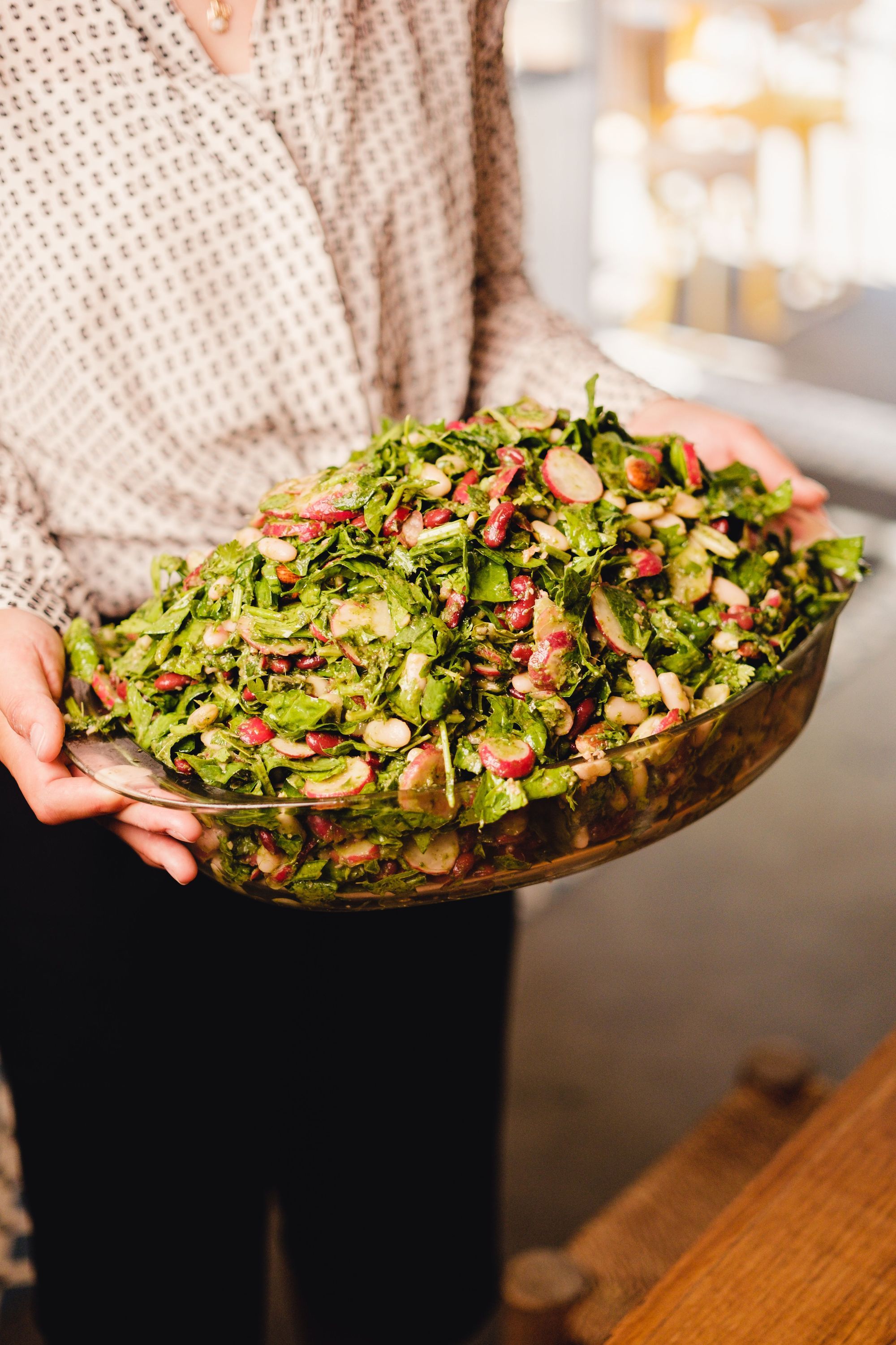 Grand plat rempli de salade végétarienne fraîche avec radis et verdure, tenu par une personne habillée en chemise à motifs.
