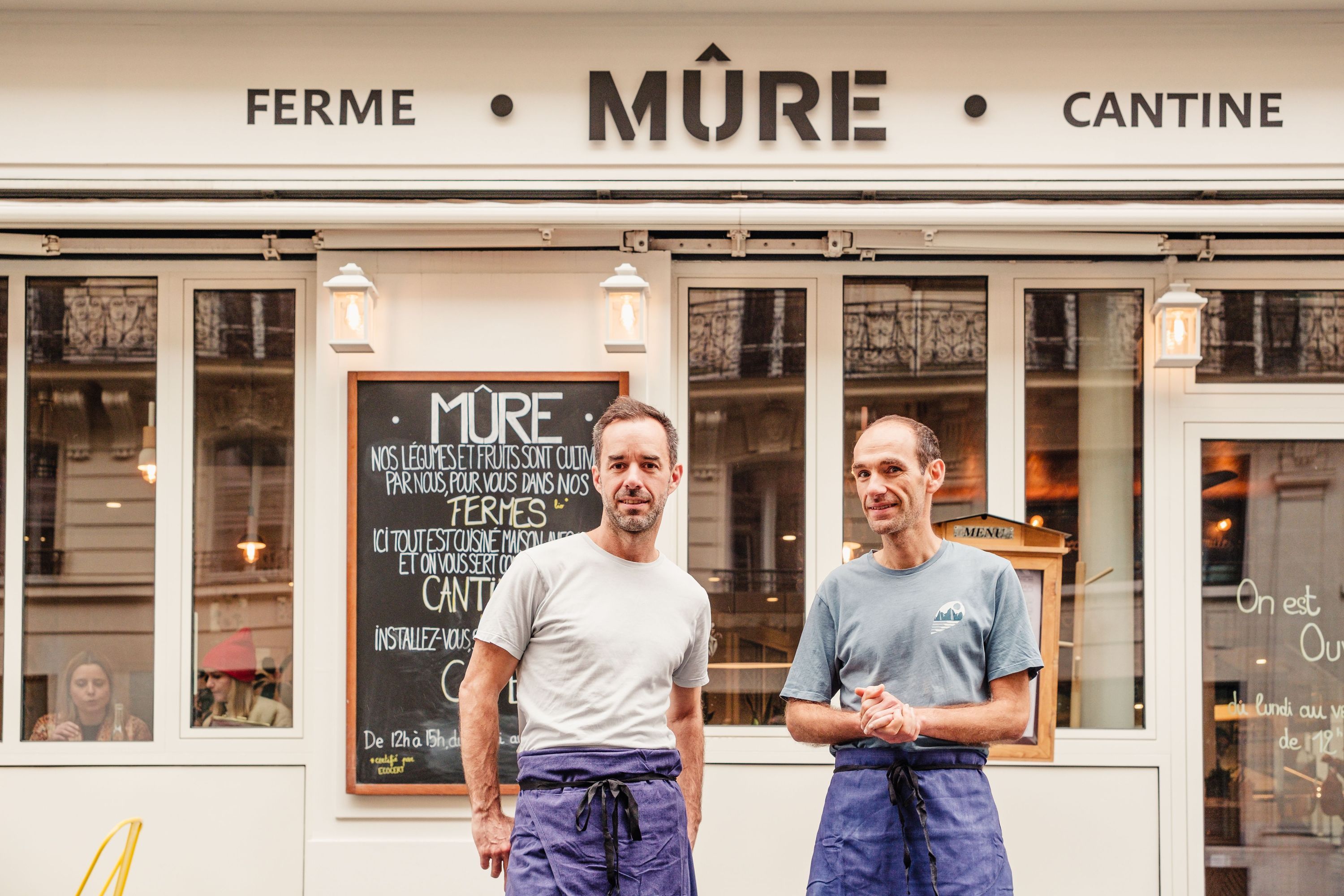 Devanture du restaurant bio MÛRE à Paris avec deux hommes en tablier bleu posant devant l'entrée.
