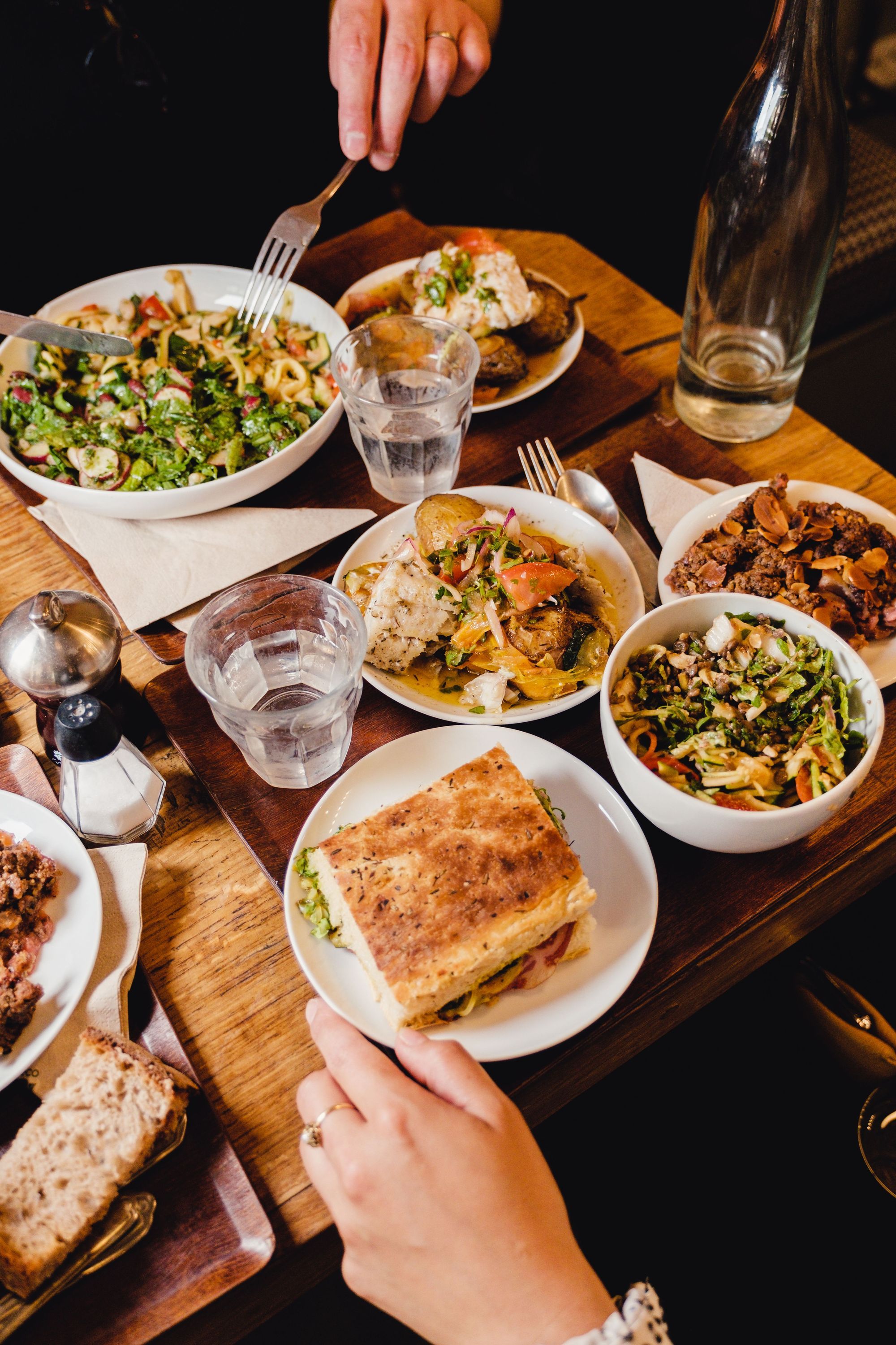 Repas variés avec salades, sandwichs et plats servis sur une table en bois, typique d'un restaurant bio à Paris.