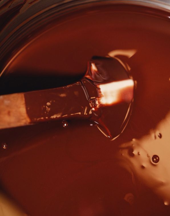 Rich melted chocolate being stirred with a wooden spatula, showing smooth texture and glossy surface.