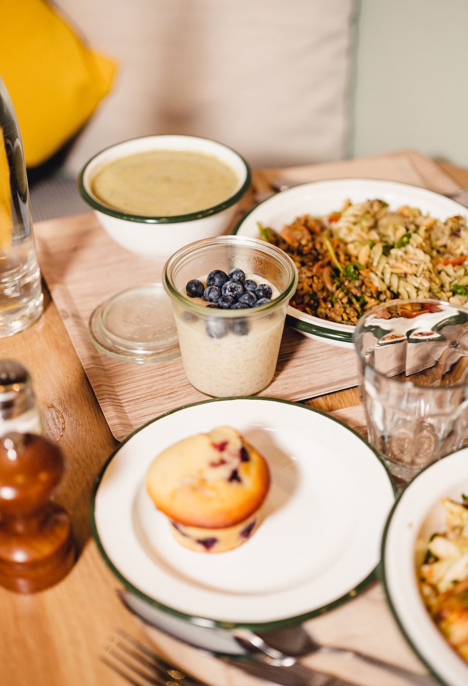 Healthy meal spread with a blueberry muffin, creamy soup, grain salad, and a glass of water on a wooden table