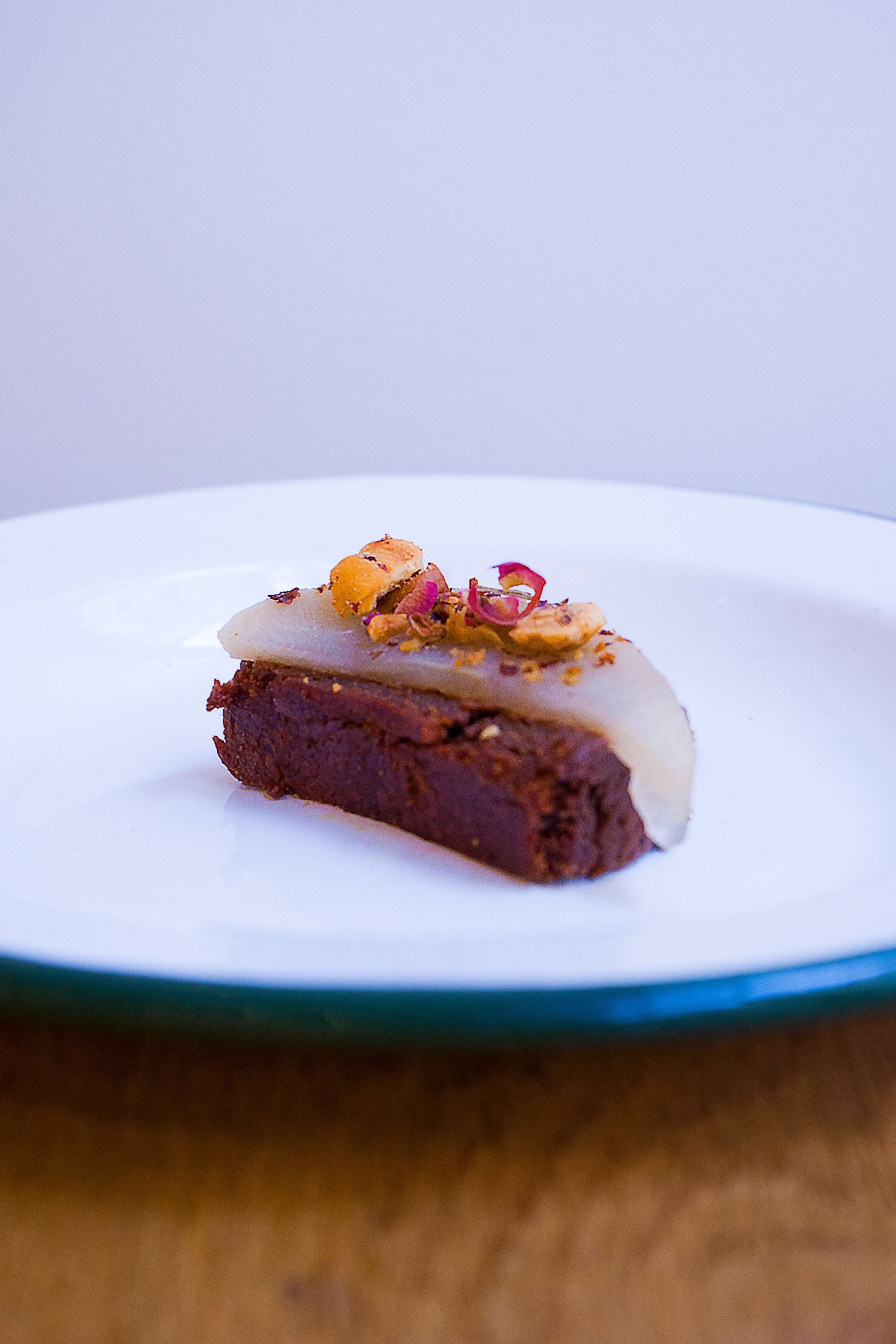 Une portion de dessert au chocolat garnie de tranches de fruit et de pétales sur une assiette blanche.