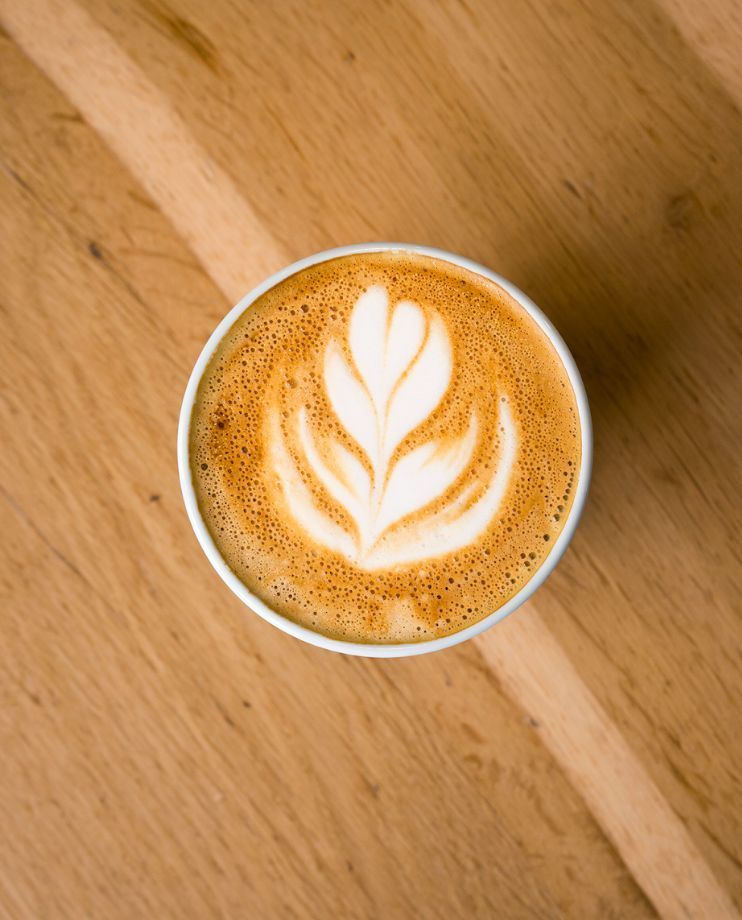 Latte art with a leaf design in a white cup on a wooden table, showcasing a creamy coffee beverage.