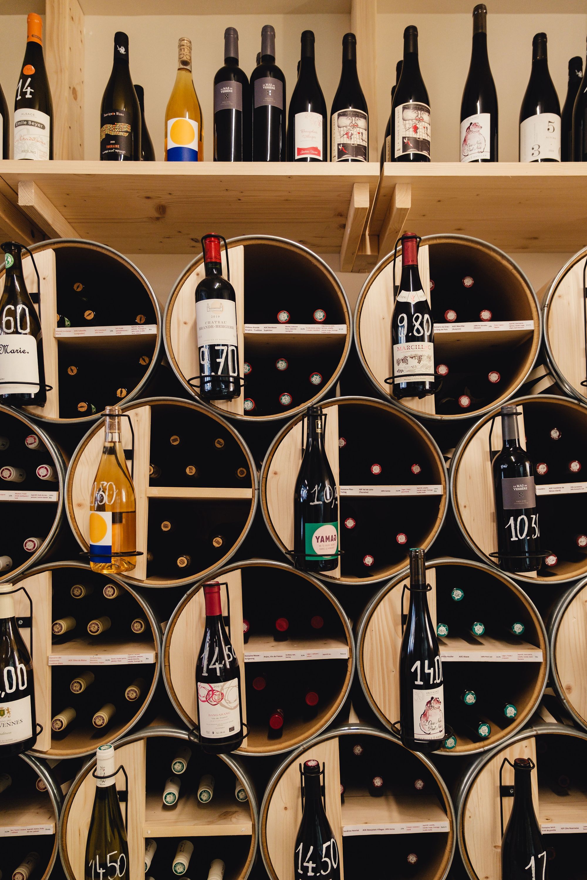 Rayonnage en bois avec bouteilles de vin variées dans des compartiments ronds au restaurant bio MURE épicerie à Paris.