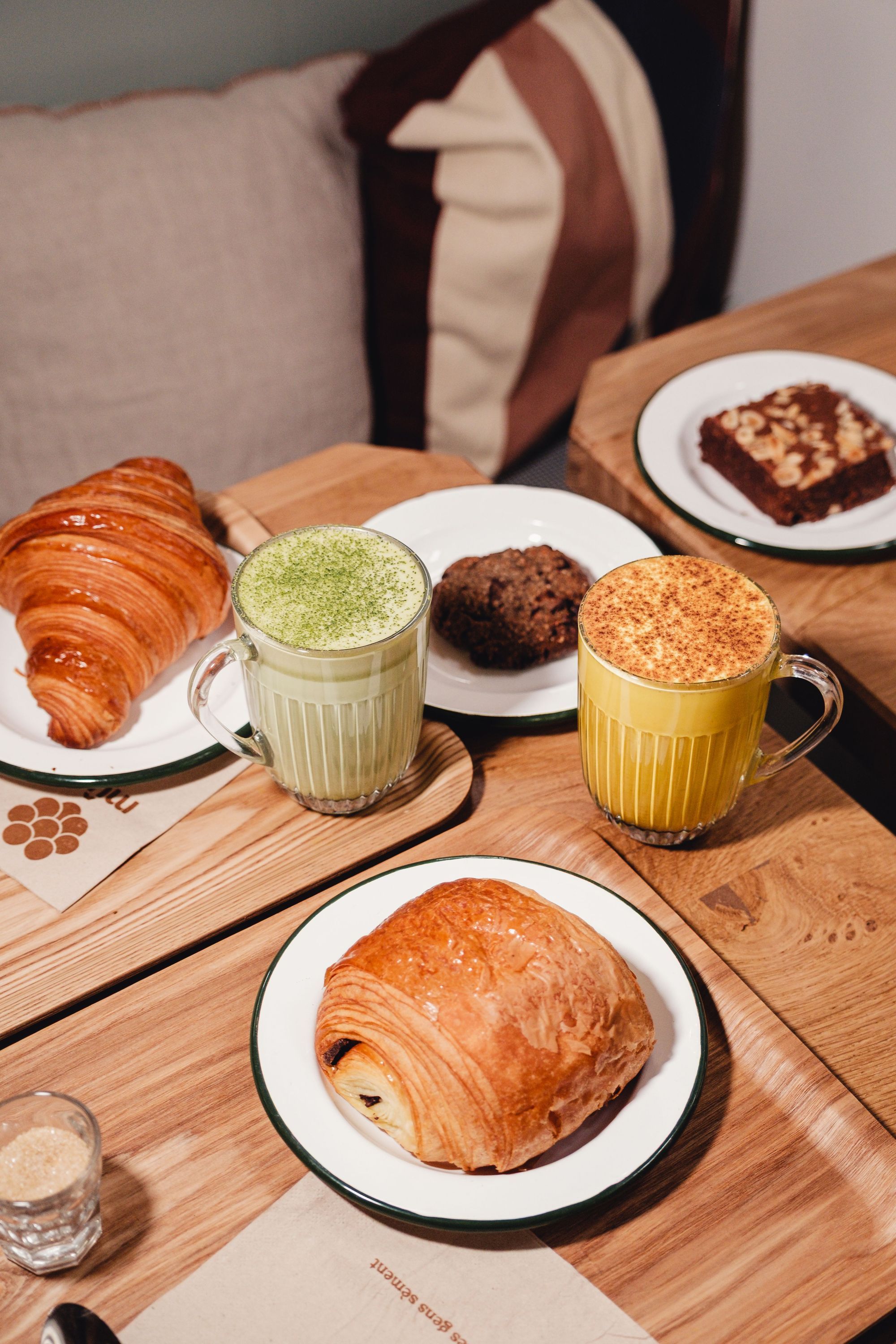Une table en bois avec des pâtisseries variées et deux boissons chaudes, dans un cadre de restaurant.