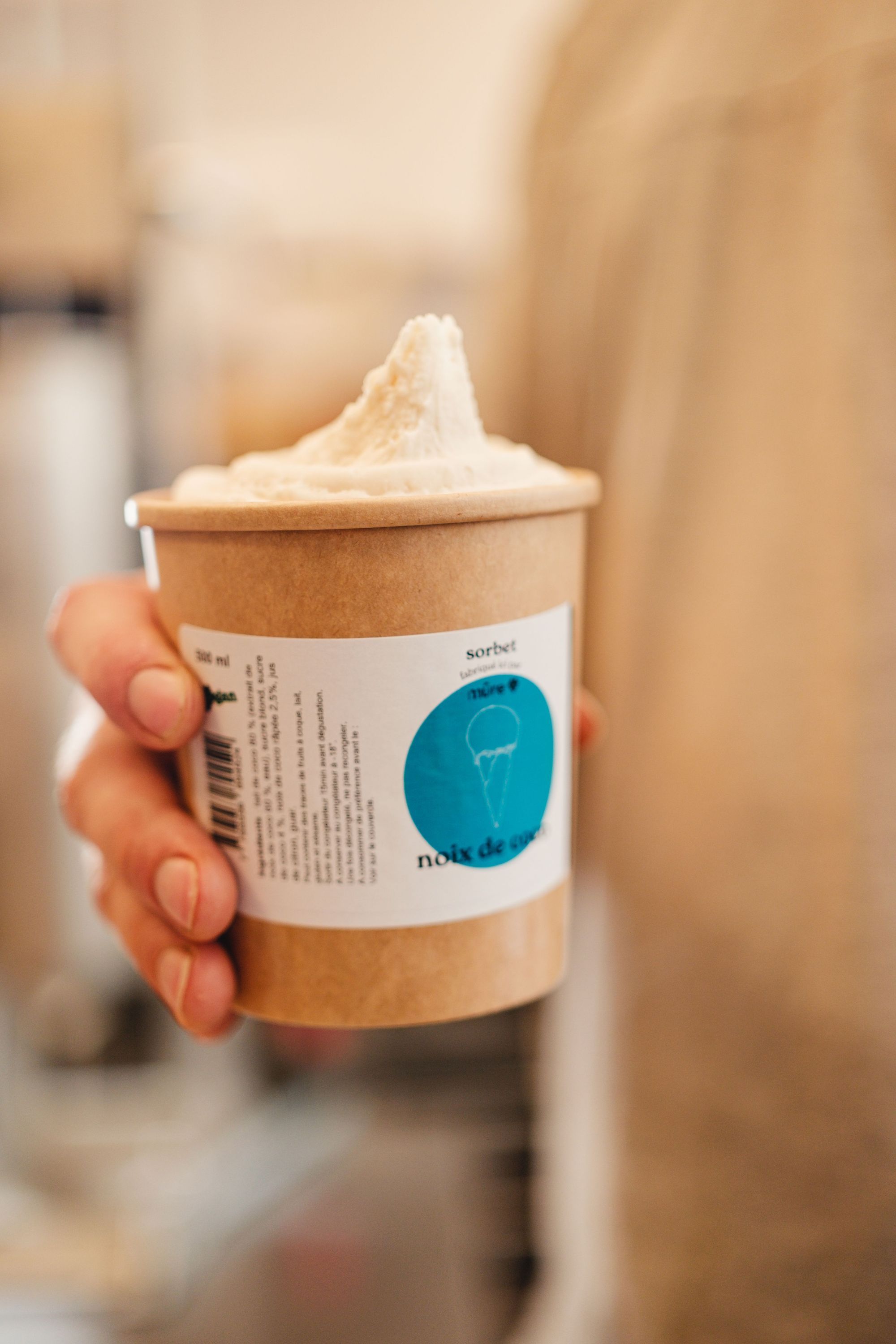 Sorbet noix de coco servi dans un pot en carton tenu à la main dans un restaurant bio à Paris.