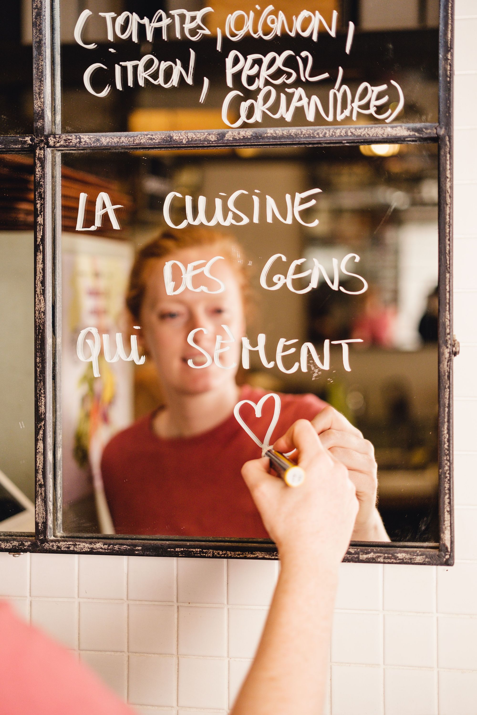 Texte écrit à la main sur un miroir avec des ingrédients et un message sur la cuisine, reflet d'une personne en arrière-plan.