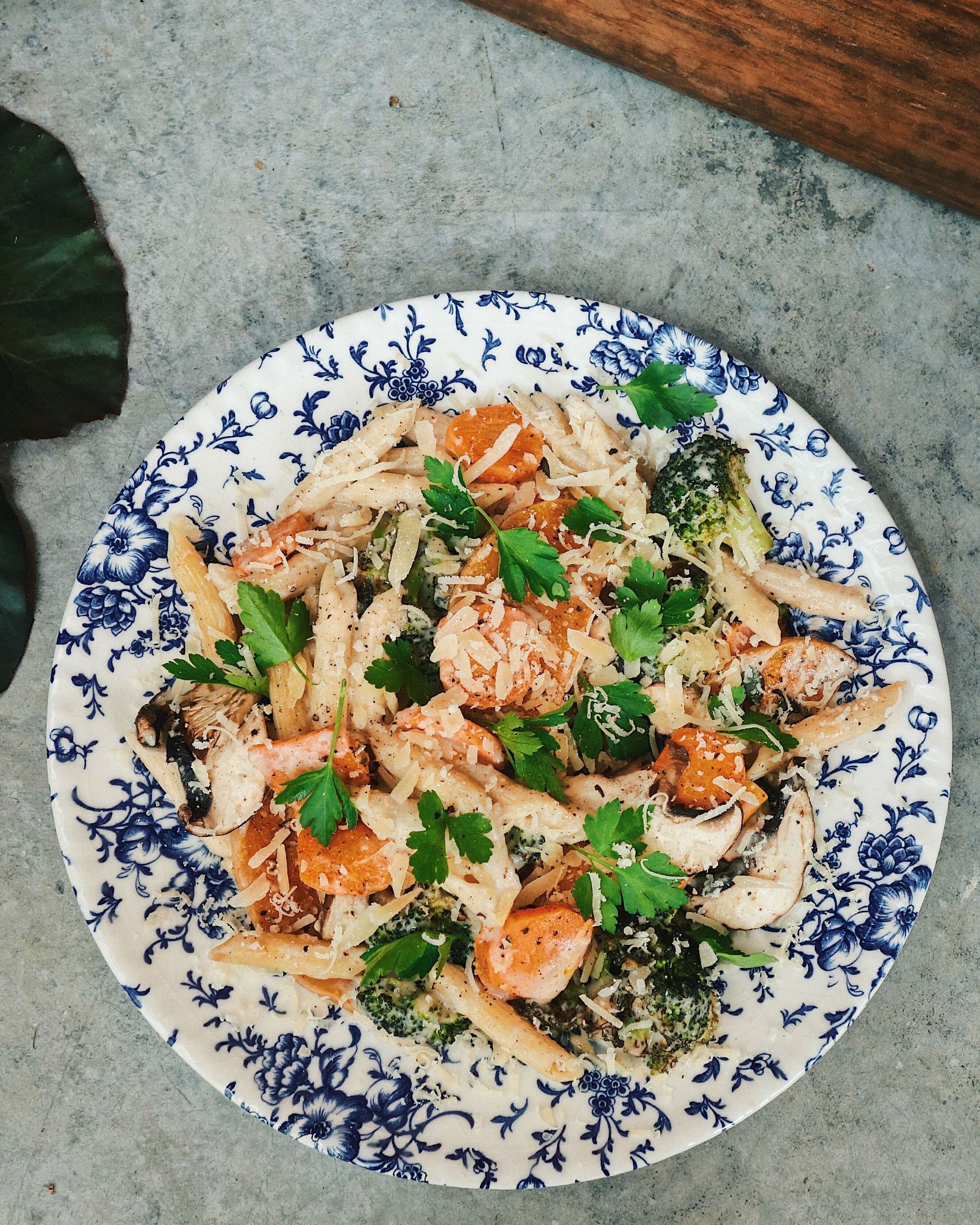 Plat végétarien sain avec pâtes, carottes, brocolis et persil servi sur une assiette bleue à motif floral.